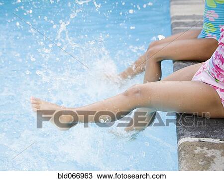 Stock Image - Hispanic girls splashing water in swimming pool. Fotosearch