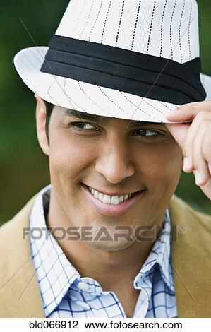 Stock Image - Hispanic man adjusting hat. Fotosearch
