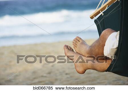 Stock Photography - Hispanic man laying in hammock at beach. Fotosearch