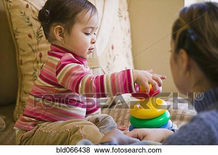 Stock Photo - Hispanic mother watching daughter stack plastic rings. Fotosearch