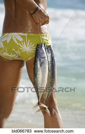 Stock Image - Man standing in ocean carrying fish. Fotosearch