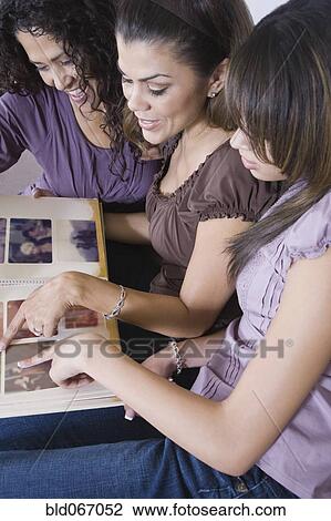 Stock Image - Multi-generational women looking at photo album. Fotosearch