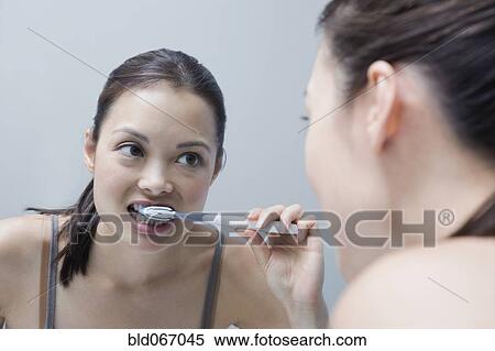 Stock Photography - Woman brushing teeth in mirror. Fotosearch