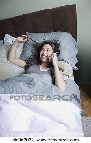 Stock Image - Woman talking on phone in bed. Fotosearch