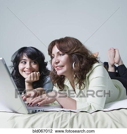 Stock Image - Young woman and mother using laptop on bed. Fotosearch