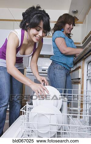 Stock Photography - Young woman helping mother load dishwasher. Fotosearch