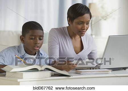 Stock Image - African boy doing homework next mother on computer. Fotosearch