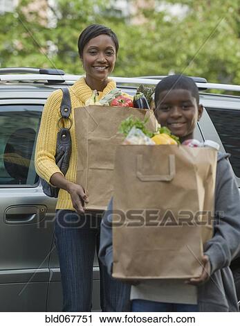 Stock Image - African boy helping mother unload groceries. Fotosearch