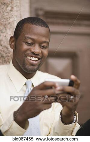 Stock Photography - African businessman sending text message. Fotosearch
