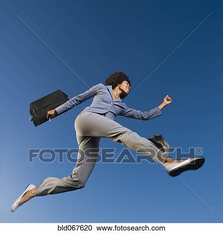 Stock Image - African businesswoman carrying briefcase in mid-air. Fotosearch