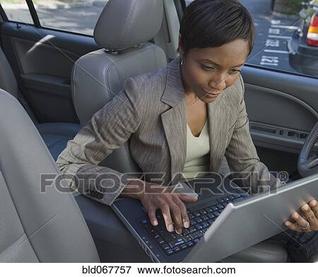 Stock Photo - African businesswoman typing on laptop in car. Fotosearch