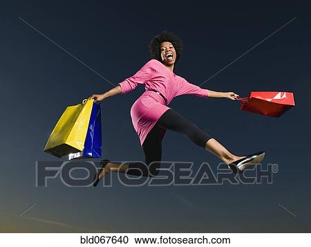 Stock Image - African woman holding shopping bags in mid-air. Fotosearch