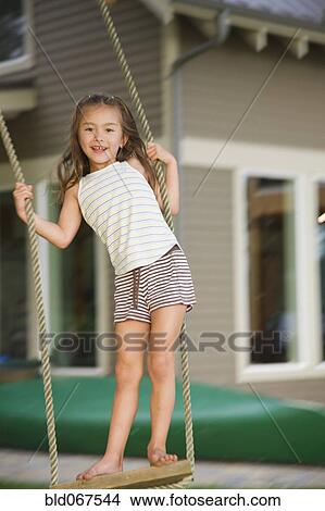 Picture - Asian girl swinging on rope swing. Fotosearch