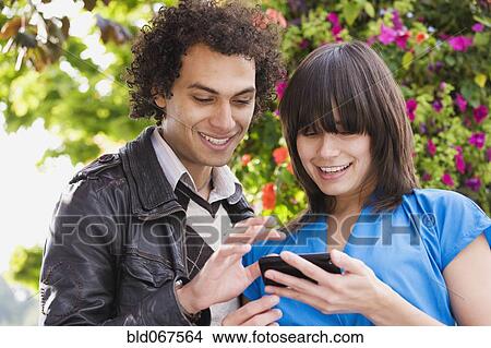 Picture - Couple text messaging on cell phone. Fotosearch