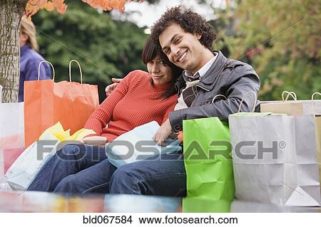 Picture - Exhausted couple sitting with shopping bags. Fotosearch