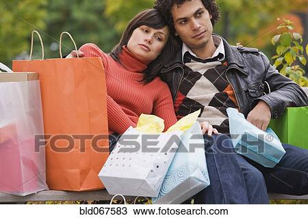 Stock Image - Exhausted couple sitting with shopping bags. Fotosearch