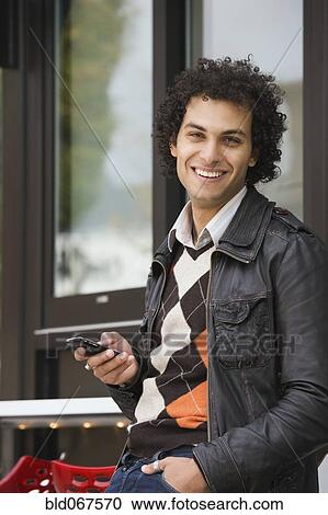 Stock Image - Middle Eastern man text messaging on cell phone. Fotosearch
