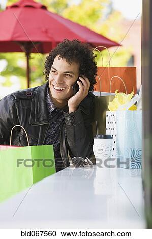 Stock Image - Middle Eastern man with shopping bags talking on cell phone. Fotosearch