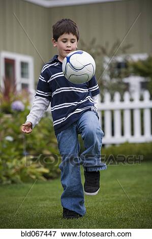 Stock Photo - Mixed race boy playing soccer in backyard. Fotosearch