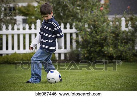 Stock Photograph - Mixed race boy playing soccer in backyard. Fotosearch