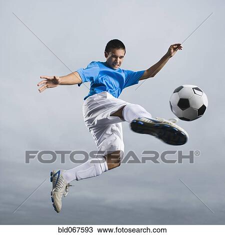 Stock Image - Mixed race teenager in mid-air kicking soccer ball. Fotosearch