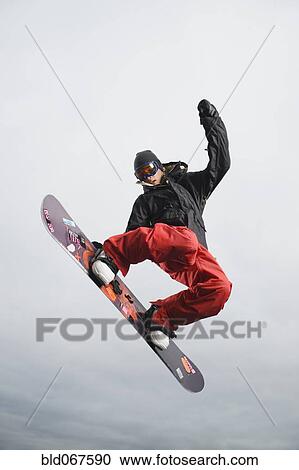 Stock Image - Mixed race teenager in mid-air on snowboard. Fotosearch
