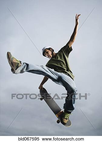 Stock Photography - Mixed race teenager in mid-air on skateboard. Fotosearch