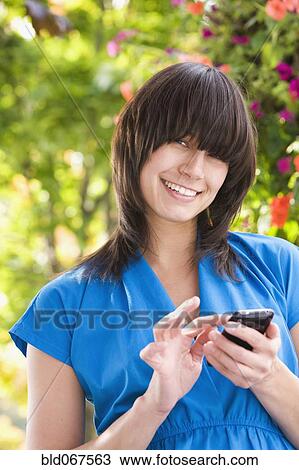 Stock Image - Mixed race woman text messaging on cell phone. Fotosearch