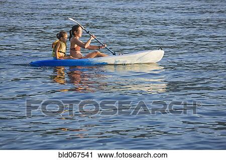 Stock Image - Mother and daughter rowing kayak on lake. Fotosearch