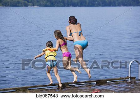 Stock Image - Mother and daughters jumping into lake. Fotosearch