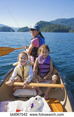 Stock Image - Mother and daughters rowing canoe on lake. Fotosearch