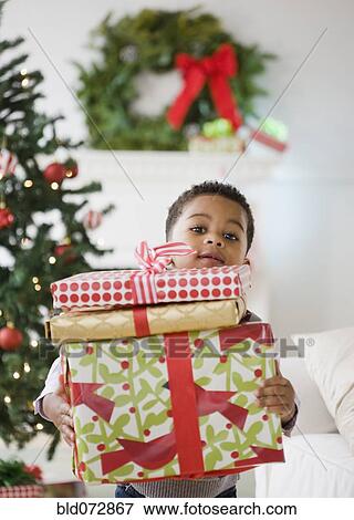 Stock Photo - African American boy holding stack of Christmas gifts. Fotosearch