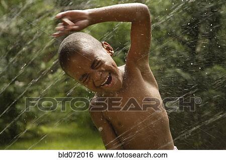 Stock Photograph - African American boy playing in sprinkler. Fotosearch