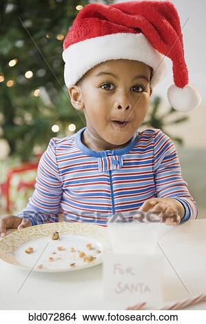 Picture - African American boy pointing to eaten cookies by 'For Santa' sign. Fotosearch