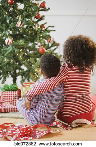 Stock Image - African American brother and sister hugging by Christmas tree. Fotosearch