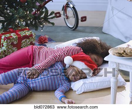 Stock Image - African American brother and sister sleeping by Christmas tree. Fotosearch