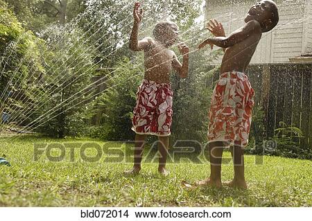 Picture - African American brothers playing in sprinkler. Fotosearch