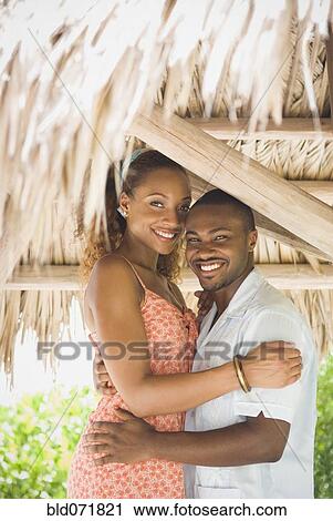 Stock Image - African American couple hugging in grass hut. Fotosearch