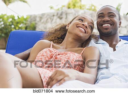 Picture - African American couple laying on lounge chair. Fotosearch