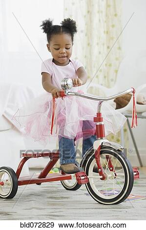 Stock Photo - African American girl in costume riding tricycle. Fotosearch