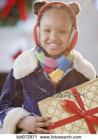 Stock Image - African American girl in earmuffs holding Christmas gift. Fotosearch