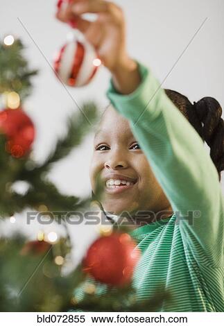 Stock Photography - African American girl putting ornament on Christmas tree. Fotosearch