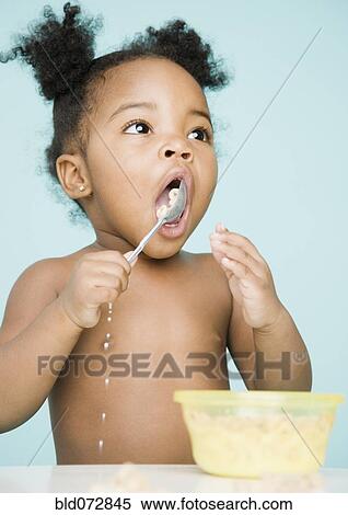 Stock Photography - African American girl trying to eat cereal with spoon. Fotosearch