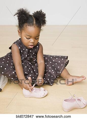 Stock Photo - African American girl trying to put shoes on. Fotosearch