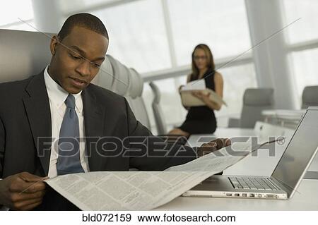 Stock Photo - African businessman reading newspaper in conference room. Fotosearch