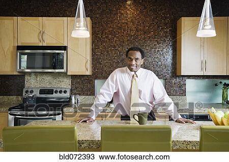 Stock Image - African businessman standing in modern kitchen. Fotosearch