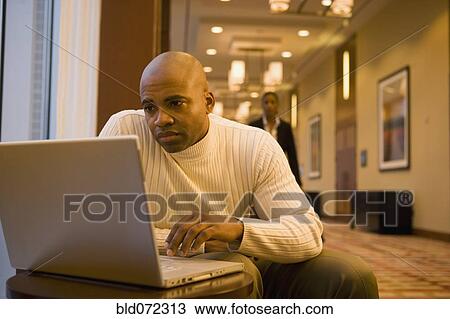 Stock Image - African businessman working on laptop in corridor. Fotosearch
