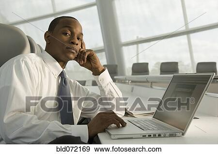 African businessman working on laptop and looking serious View Large Photo Image Stock Photo - African businessman working on laptop and looking serious. Fotosearch