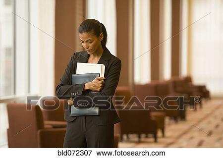 Stock Photo - African businesswoman holding paperwork in hotel lobby. Fotosearch