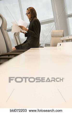 Stock Image - African businesswoman reviewing paperwork in conference room. Fotosearch